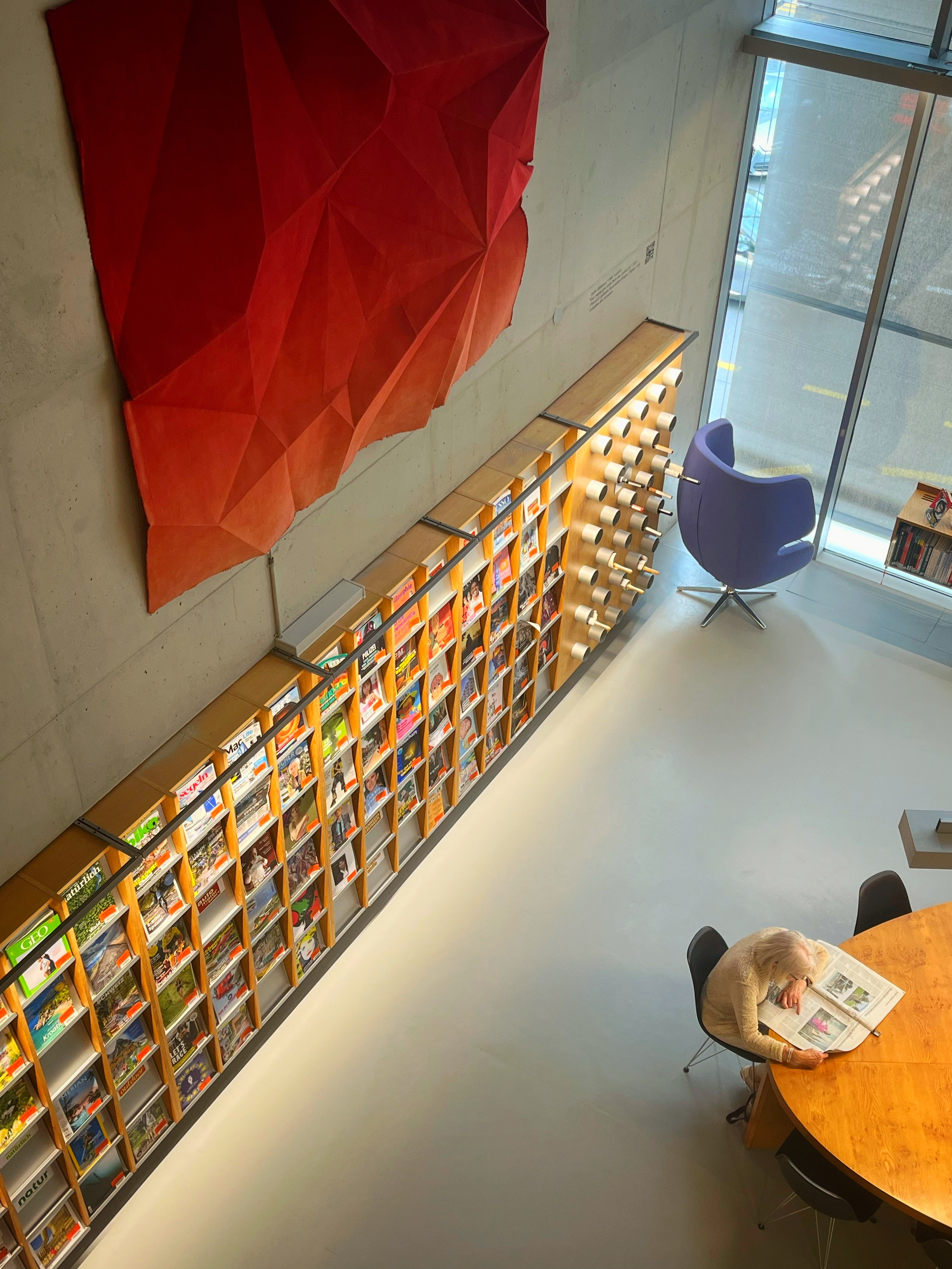 Bird's-eye view of Lucerne library, magazine wall, red sculpture, a lone reader below