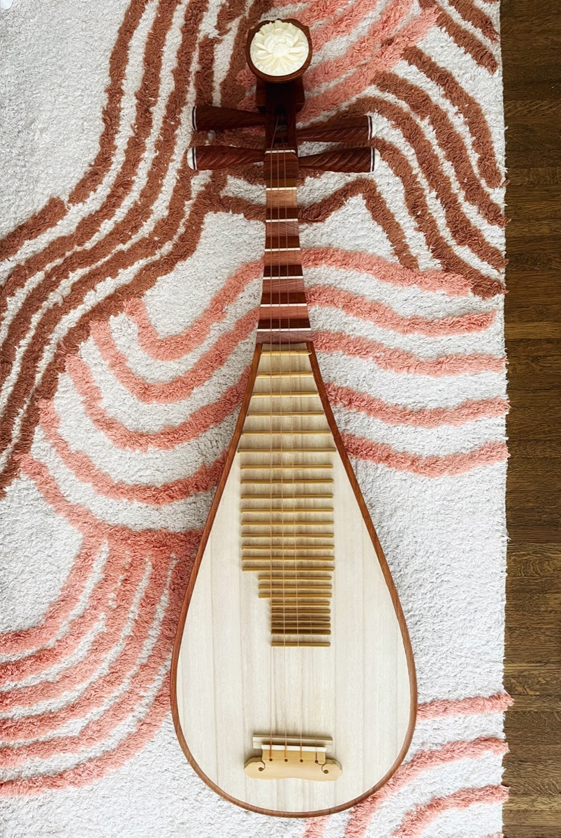 A hand-crafted pipa laid on a pink patterned rug