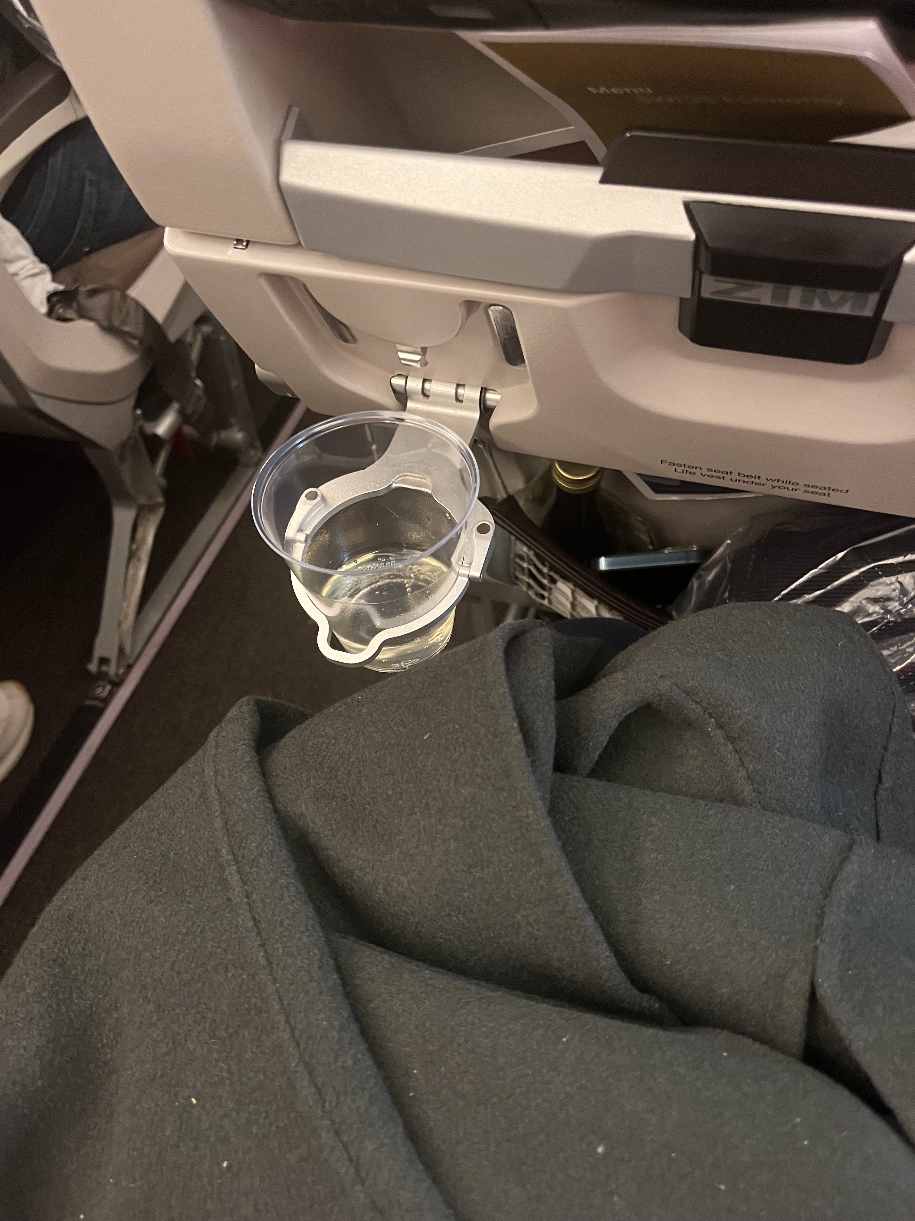 A plastic cup on an airplane tray table, dark coat folded below
